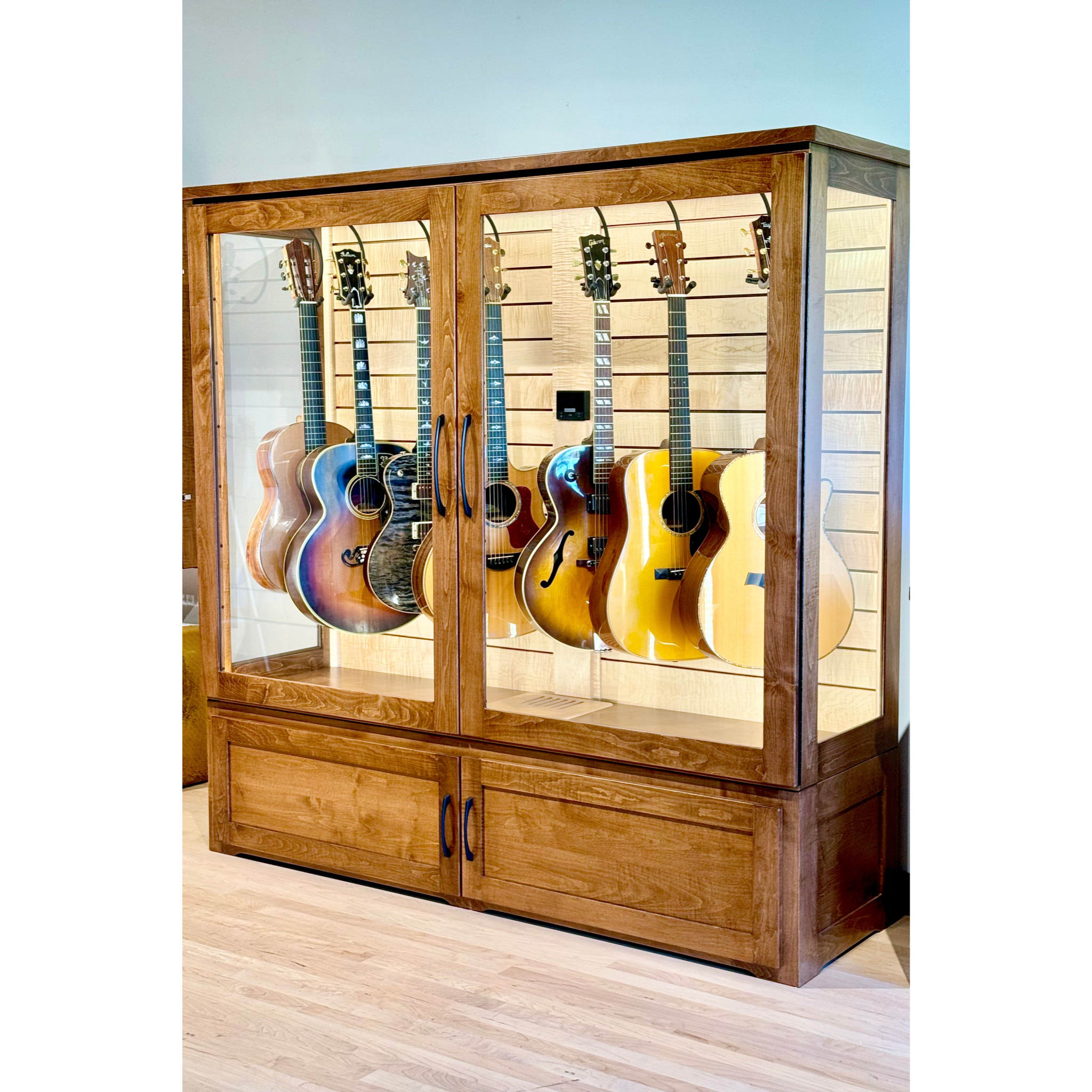 Wooden display cabinet with glass doors showcasing six guitars on a light blue background.